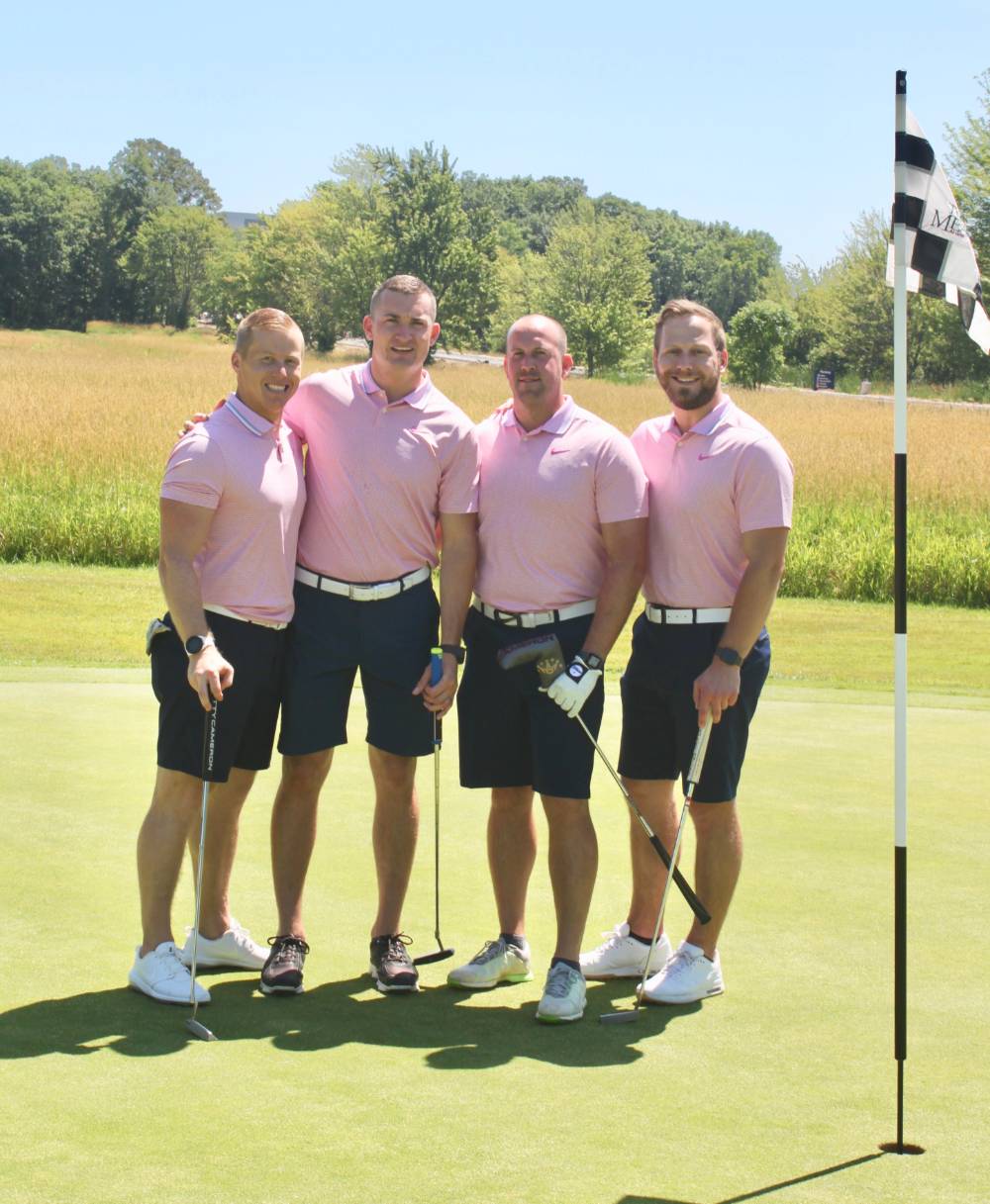 4 team members pose for a picture on the green in pink shirts